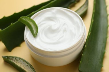 Kavanozda aloe vera özütüyle nemlendirici krem ve sarı arkaplanda yapraklar, yakın plan