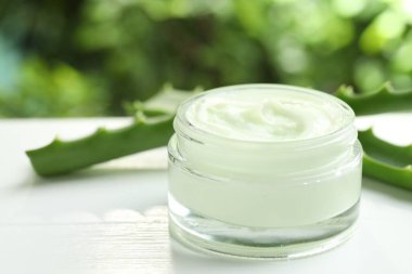 Kavanozda aloe vera özütüyle nemlendirici krem ve beyaz ahşap masa üzerindeki yaprakları bulanık yeşil arka planda, yakın plan
