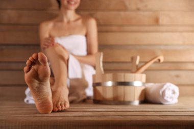 Saunada banyo malzemeleriyle bankta dinlenen gülümseyen kadın, yakın plan. Seçici odak