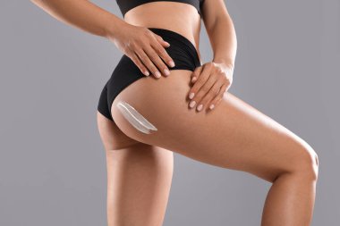 Gri arka plana anti-selülit kremi süren kadın, yakın plan.