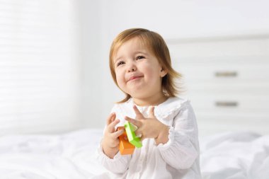 Sevimli küçük kız evde yatakta oyuncakla oynuyor.