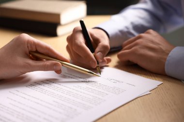 Kadın belgeye işaret ediyor ve adam ahşap masaya imza atıyor, yakın plan.