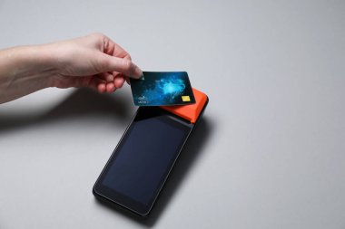 Kredi kartı olan bir kadın gri arka planda ödeme terminalini kullanıyor. Metin için boşluk