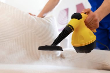 Temizlikçi kanepeyi evde buharlı temizleme makinesiyle temizliyor.