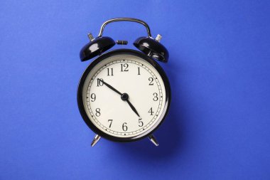 Mavi arkaplanda bir siyah alarm saati, üst görünümde.