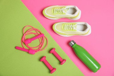 İp atlama, paspas, spor ayakkabı, su şişesi ve pembe arka planda dambıllar, düz uzanma. Spor malzemeleri.