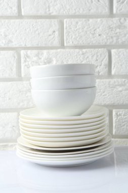 Different clean dishware on white table near brick wall
