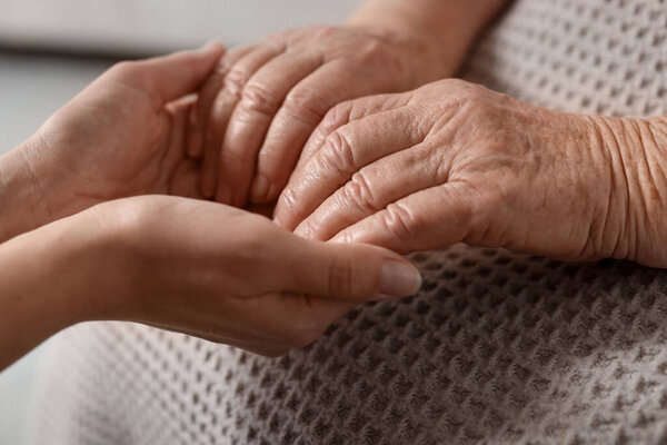 Caregiver supporting senior woman on light background, closeup. Elderly care