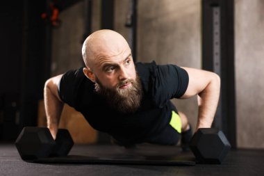 Sporcu spor salonunda halterli şınav çekiyor.