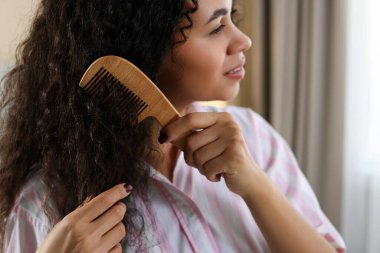 Genç bir kadın kıvırcık saçlarını içeride tarıyor, yakından. Seçici odak