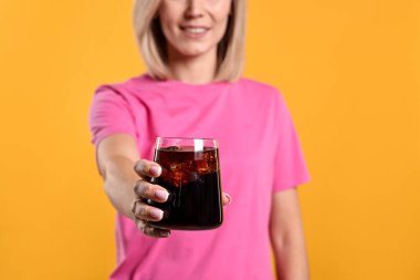 Turuncu arka planda bir bardak canlandırıcı soda içen kadın, yakın plan.