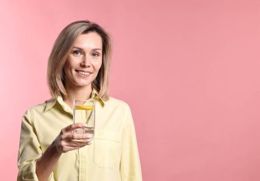 Pembe arka planda bir bardak limonata olan kadın. Tazeleyici içecek.