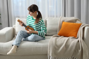 Evdeki kanepede ukulele çalan mutlu kadın.