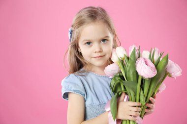 Pembe arka planda bir buket güzel bahar çiçeğiyle sevimli küçük bir kız.
