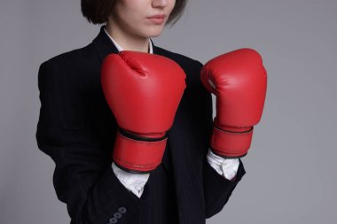 Rekabet. Takım elbiseli iş kadını gri arka planda boks eldiveni giyiyor. Kısa mesaj için yeri var.