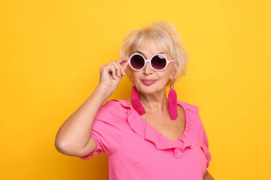 Turuncu arka planda güneş gözlüklü modaya uygun büyükannenin portresi.