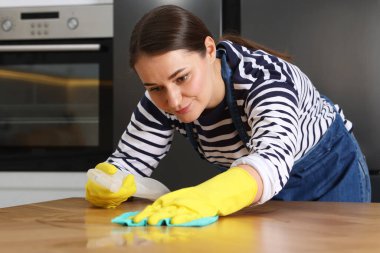 İçerideki bez parçasıyla ahşap masayı silerken temizlik malzemesi kullanan kadın.