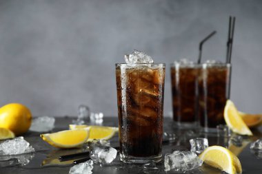 Koyu gri masada taze buzlu kola ve limon dilimleri. Metin için boşluk