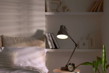 İçerideki komodinin üzerinde parlayan gece lambası ve çalar saat.