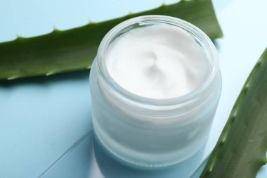 Açık mavi arkaplanda krema ve aloe yaprakları, yakın plan