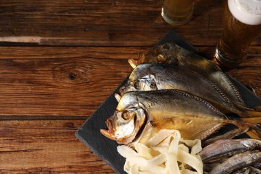 Farklı kurutulmuş balık atıştırmalıkları ve ahşap masada bira, manzaranın üstünde. Metin için boşluk
