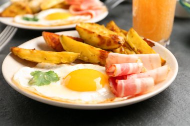 Lezzetli bir kahvaltı. Koyu dokulu masada kızarmış yumurta, patates ve pastırma, yakın plan.