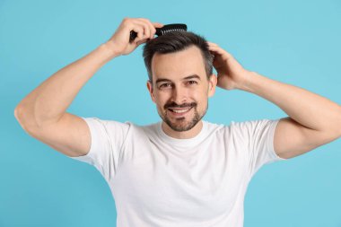 Yakışıklı adam saçlarını açık mavi arka planda tarak ile tarıyor.