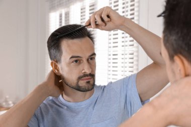 Yakışıklı bir adam saçını aynanın yanında tarıyor.