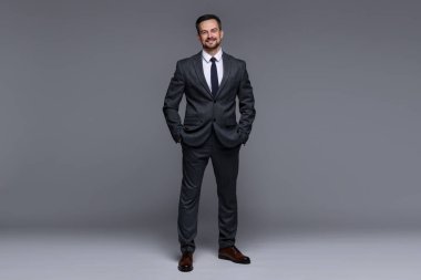 Gri arka planda klasik takım elbiseli yakışıklı bir adam.
