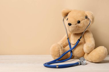 Pediatri konsepti. Tahta masadaki steteskoplu oyuncak ayı bej arkaplan, metin için boşluk