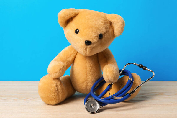 Pediatrics concept. Teddy bear with stethoscope on wooden table against light blue background