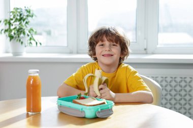 Okuldaki ahşap masada yemek yiyen şirin küçük çocuk.