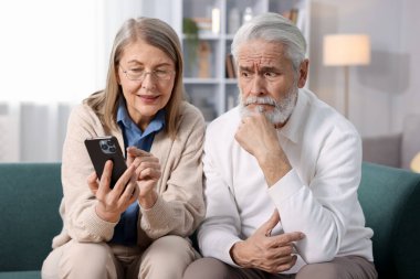 Evdeki kanepede akıllı telefonları olan sevimli yaşlı çift.