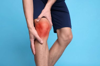 Açık mavi arka planda dizinde ağrıdan muzdarip genç adam, yakın plan