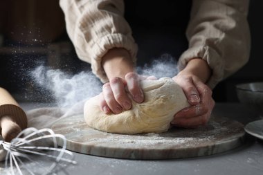 Gri masada hamur yoğuran kadın, yakın plan. Un bulutu