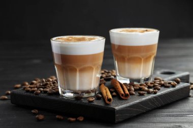 Bardakta latte macchiato, kahve çekirdekleri ve siyah ahşap masada tarçın, yakın plan.