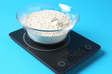 Açık mavi zemin üzerinde un bulunan elektronik mutfak terazisi, yakın plan.