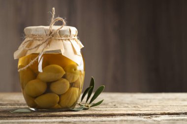Cam kavanozda yeşil zeytin turşusu ve ahşap masada yapraklar. Metin için boşluk