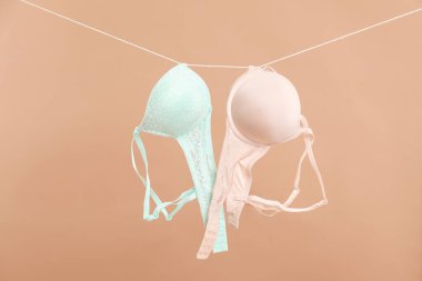 Beautiful bras hanging on rope against dark beige background