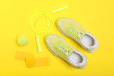 Farklı spor aletleri ve sarı arka planda spor ayakkabıları, düz yatış