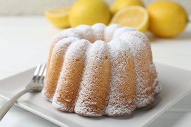 Beyaz ahşap masada pudra şekerli ve çatallı leziz limonlu pasta, yakın plan.