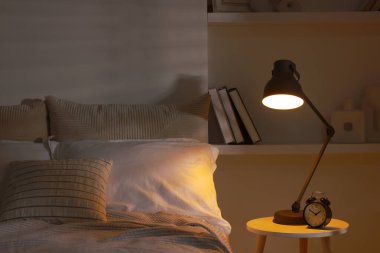 İçerideki komodinin üzerinde parlayan gece lambası ve çalar saat.