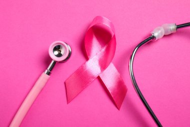 Göğüs kanseri farkındalığı. Renk arkaplanı üzerine pembe kurdele ve steteskop, üst görünüm