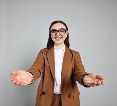 Gri arka planda müşterileri veya ortakları karşılayan mutlu iş kadını