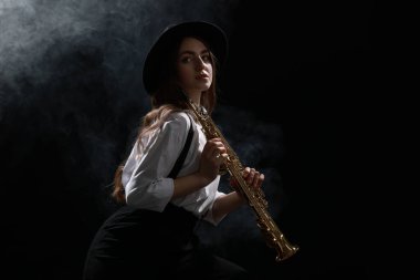 Karanlık arka planda dumanla soprano saksafon çalan müzisyen.