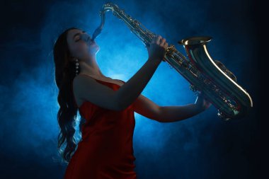 Profesyonel müzisyen koyu arkaplanda mavi ışık ve dumanla saksafon çalıyor.
