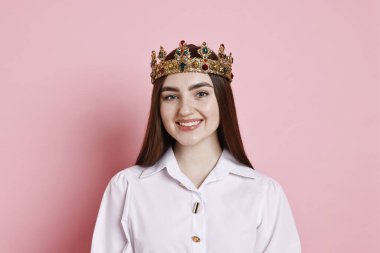 Pembe arka planda zarif taç giyen mutlu kadın.