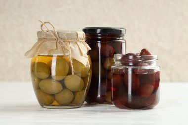 Pickled olives in glass jars on white wooden table