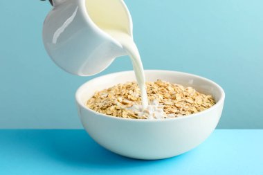 Açık mavi masada yulaf ezmesi ile sütü kaseye boşalt, yakın plan.