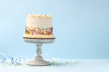 Açık mavi masaya renkli şekerlemeler serpiştirilmiş nefis bento keki, metin için yer.